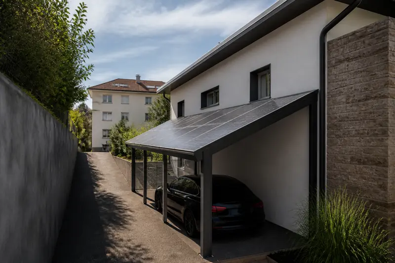 Abri de voiture en acier couvert de panneaux solaires dans une cour étroite